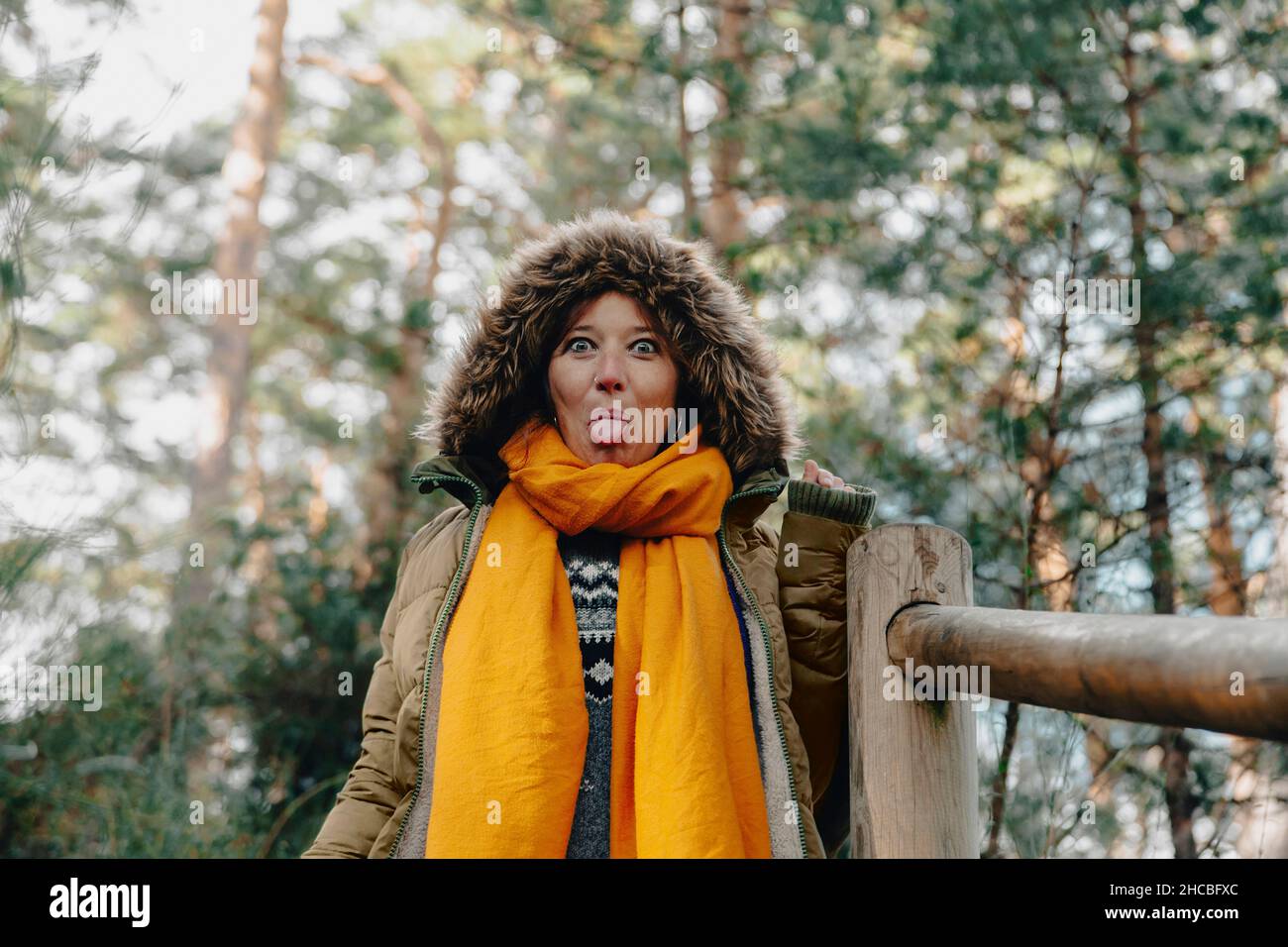 Donna in pelliccia cappuccio che sporge lingua da ringhiera a foresta Foto Stock