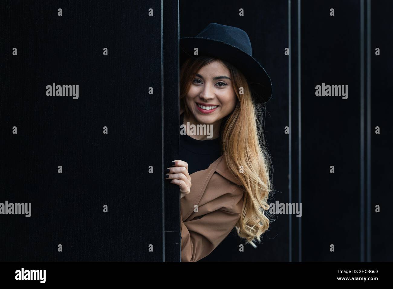 Donna bionda con cappello dietro la parete nera Foto Stock
