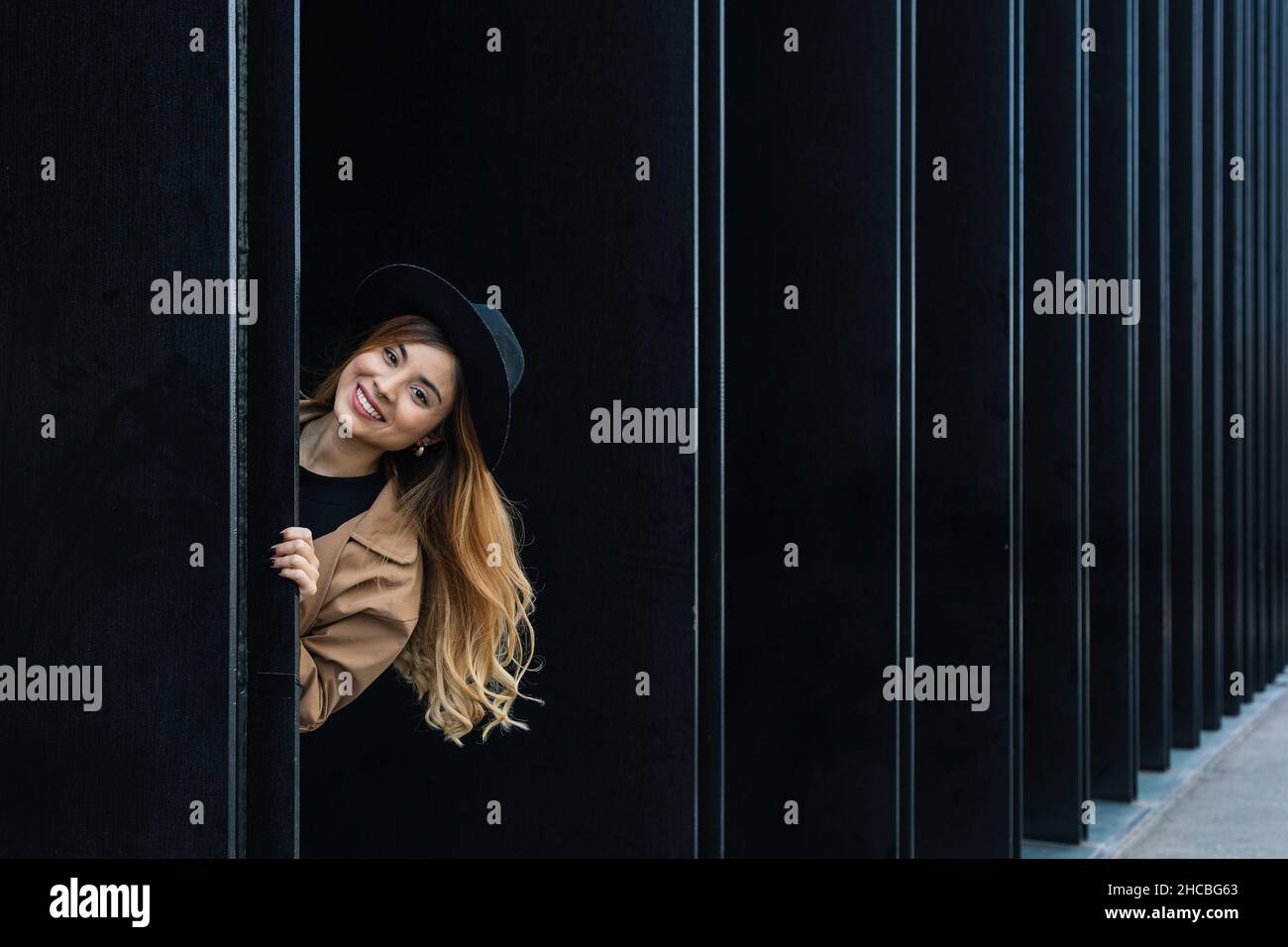 Donna giocosa sorridente dietro il muro nero Foto Stock