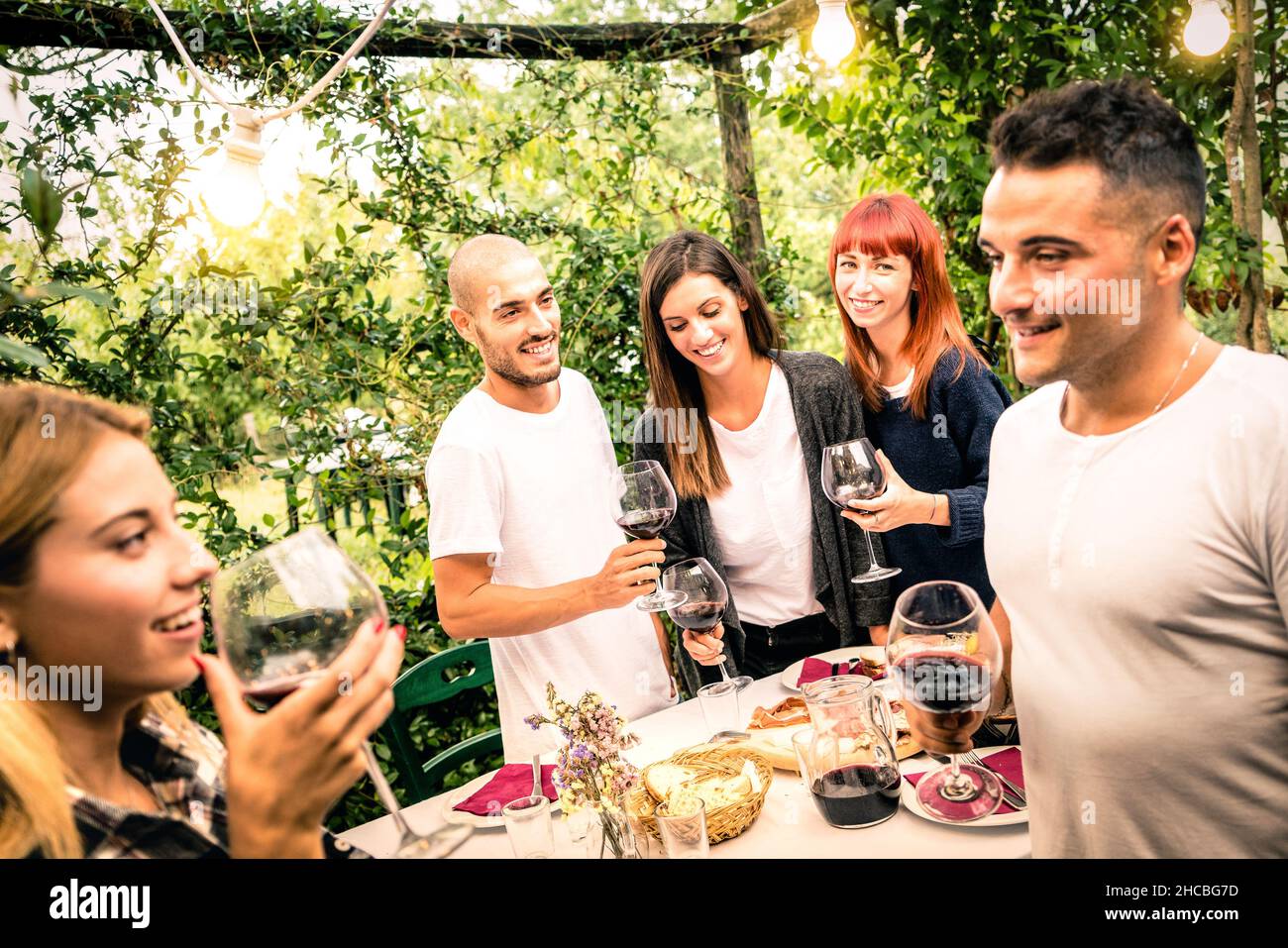 Amici felici divertirsi bevendo vino rosso a festa giardino cortile - concetto di gioventù e amicizia insieme alla cantina fattoria vigneto Foto Stock