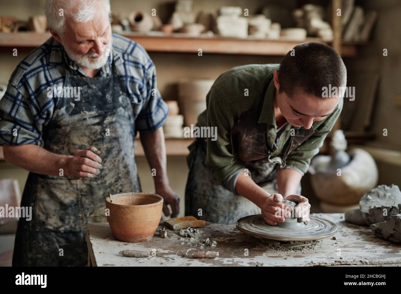 Donna artista che forma e scultura vaso vasaio di argilla cruda insieme con uomo anziano che la assiste nello studio Foto Stock