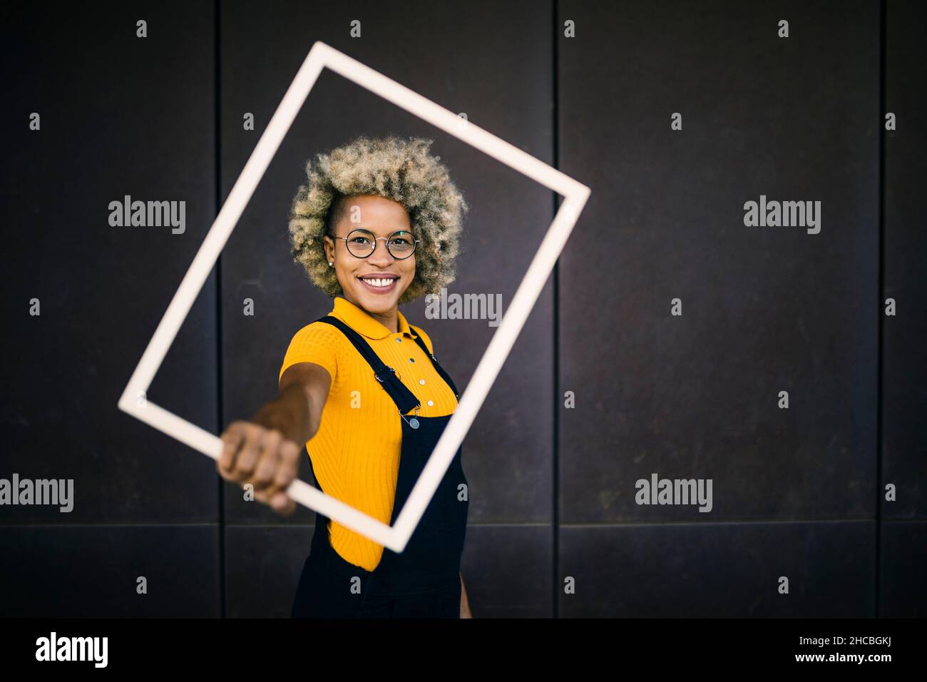 Donna felice con cornice rettangolare di fronte al muro nero Foto Stock