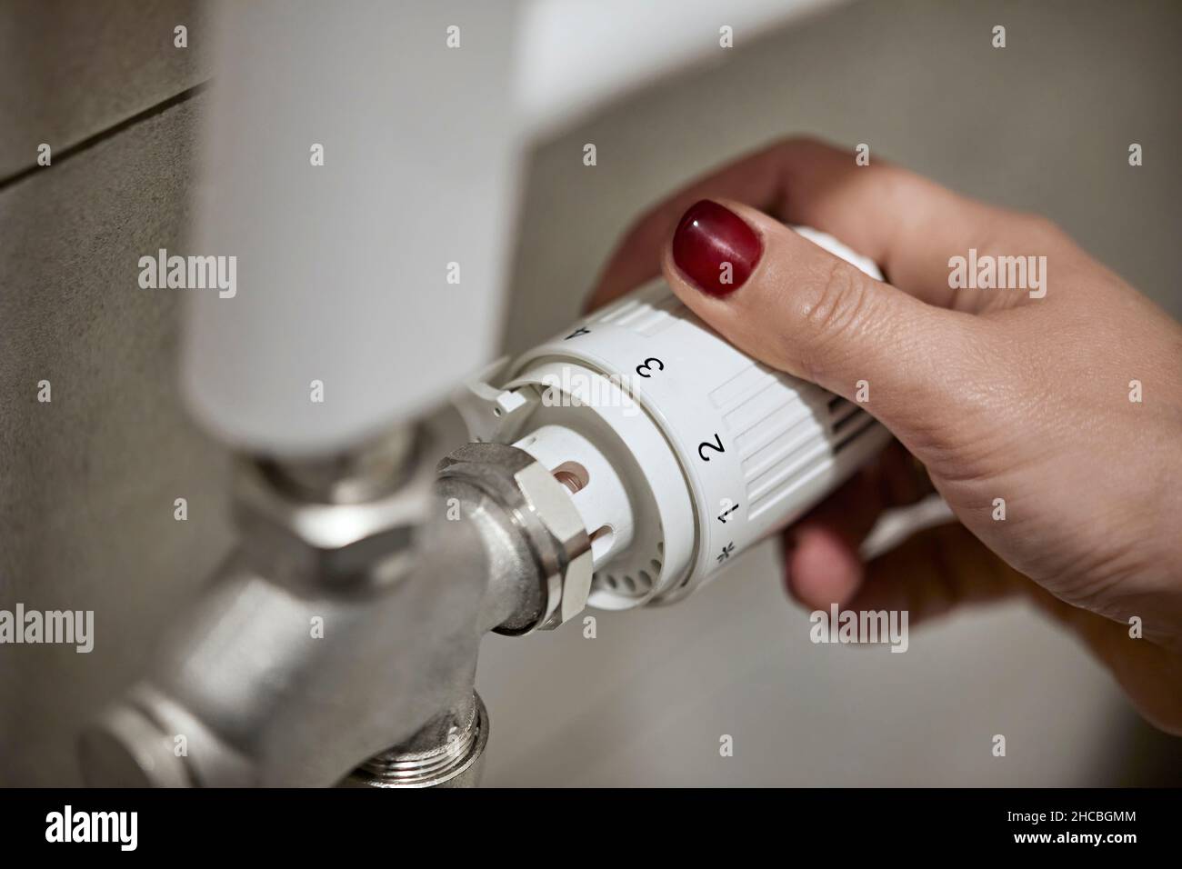 Donna che regola la valvola termostatica del radiatore della caldaia di riscaldamento a casa Foto Stock