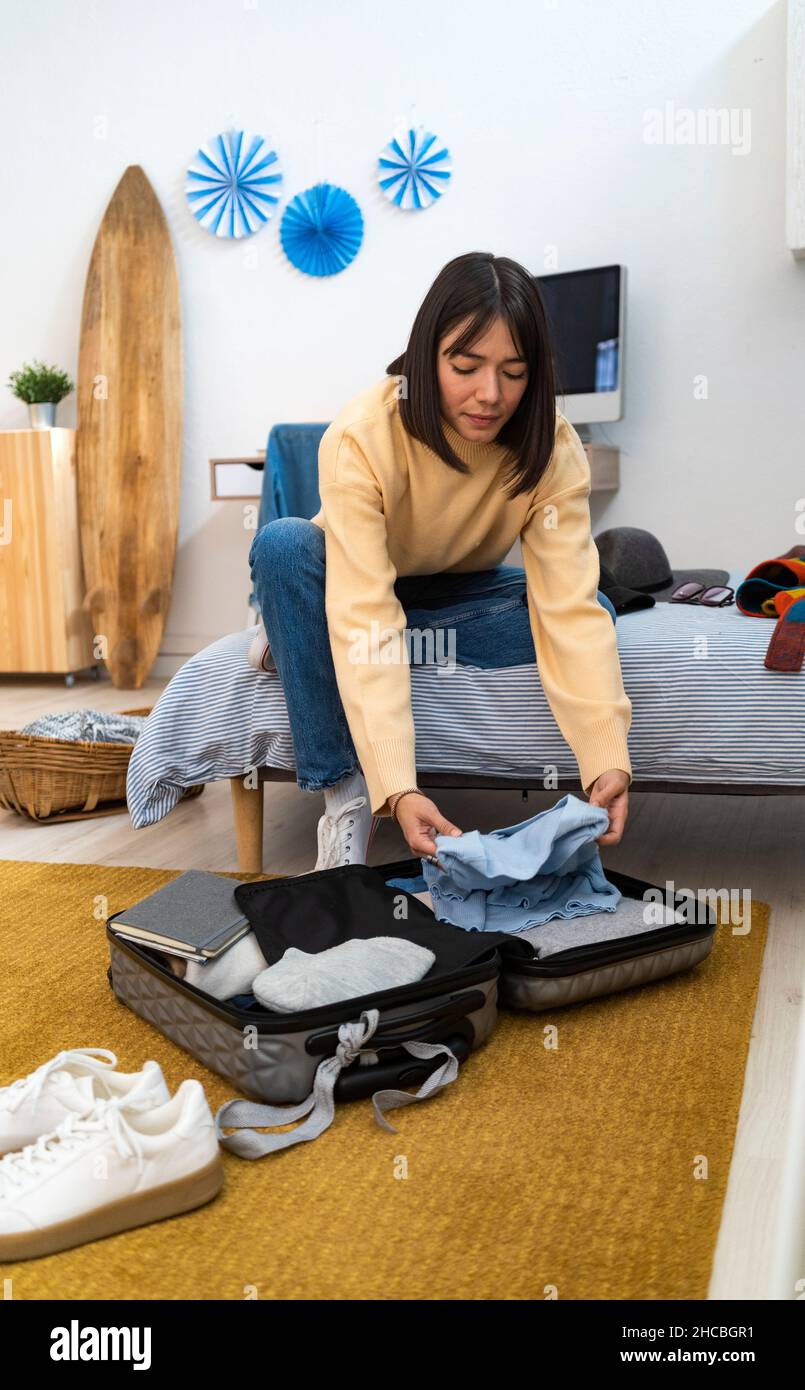 Giovane donna che porta abiti in valigia a casa Foto Stock