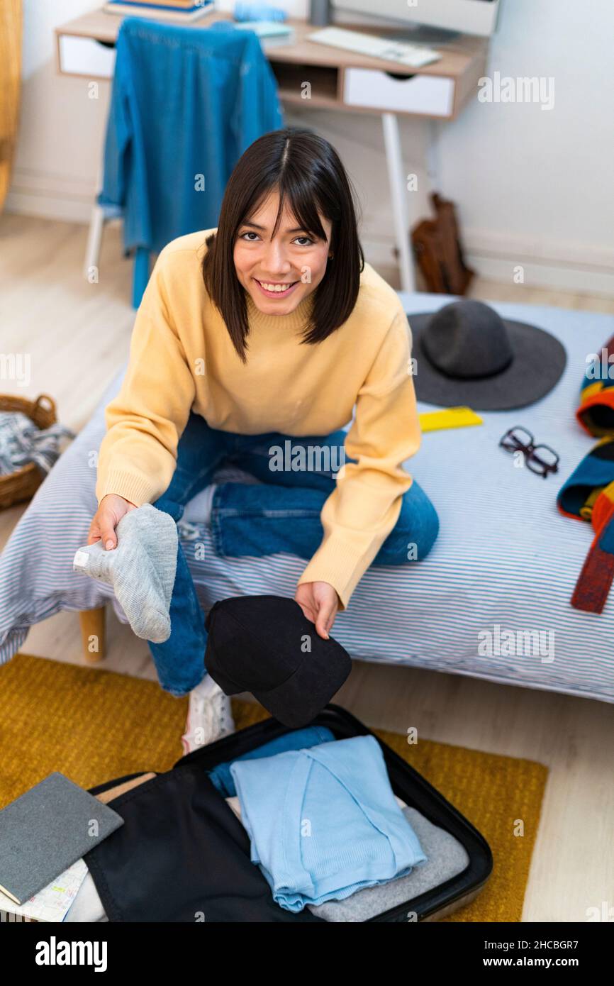 Donna sorridente che impacchettava in camera da letto a casa Foto Stock