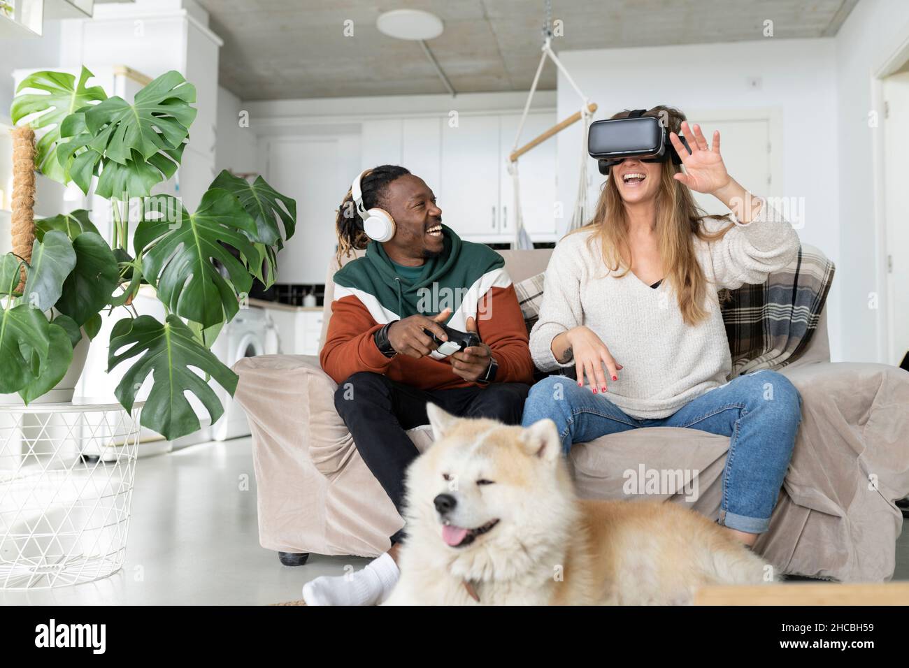 Coppia allegra che gioca il video gioco di fronte al cane a casa Foto Stock
