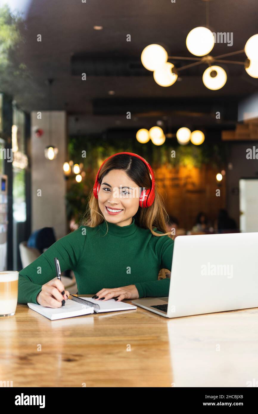Un freelance sorridente con un computer portatile e un diario al tavolo del caffè Foto Stock