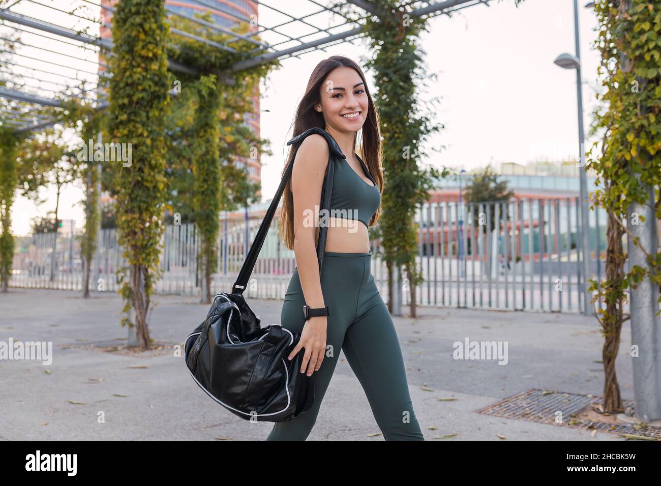 Sportswoman sorridente con sacco da palestra a piedi al parco Foto Stock