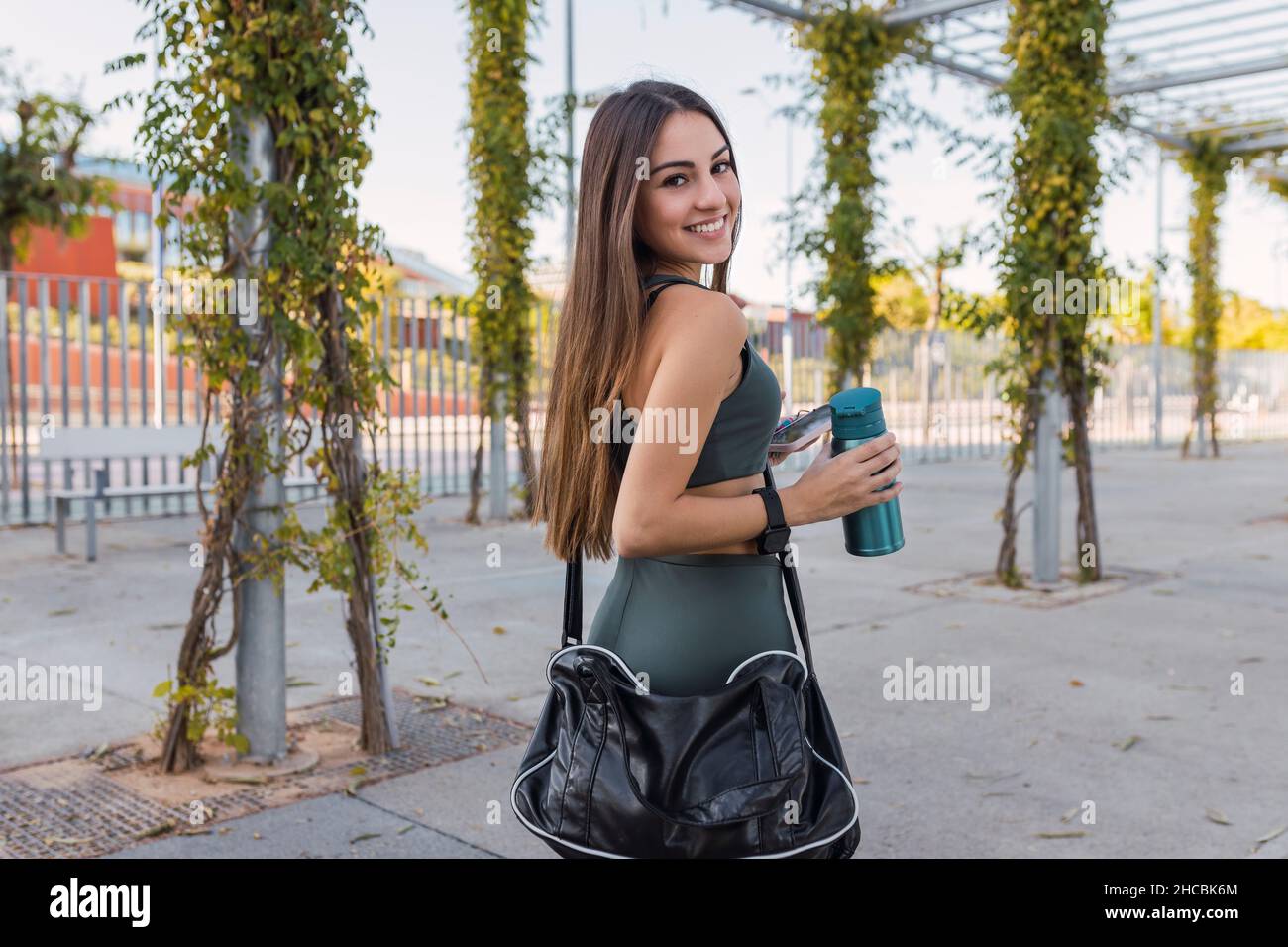 Atleta sorridente con bottiglia d'acqua che si affaccia sulle spalle nel parco pubblico Foto Stock