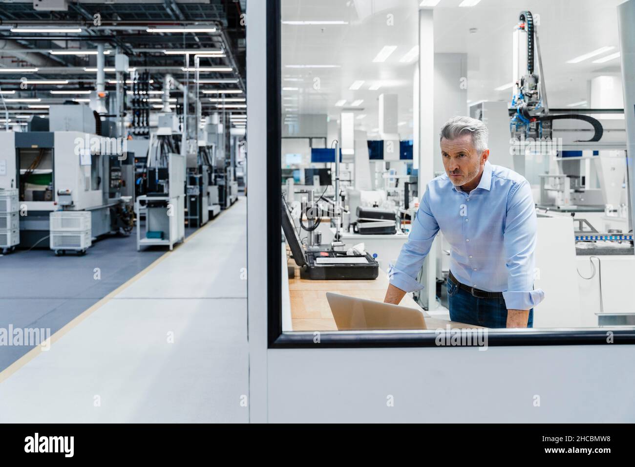 Uomo d'affari sicuro che guarda attraverso il vetro in fabbrica Foto Stock