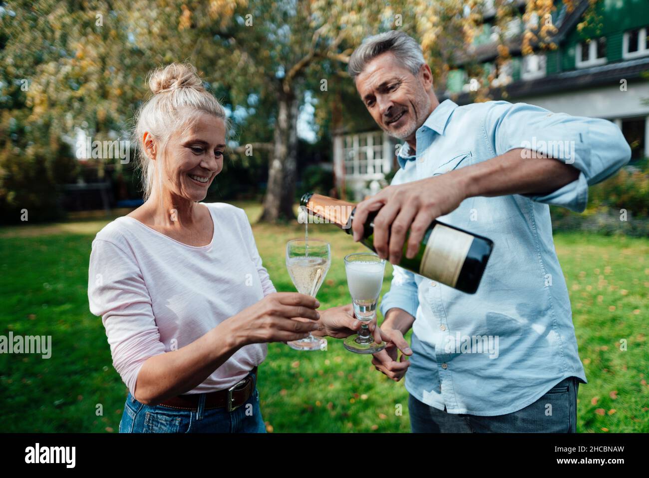 Uomo sorridente che versa champagne in flauto per la donna in cortile Foto Stock