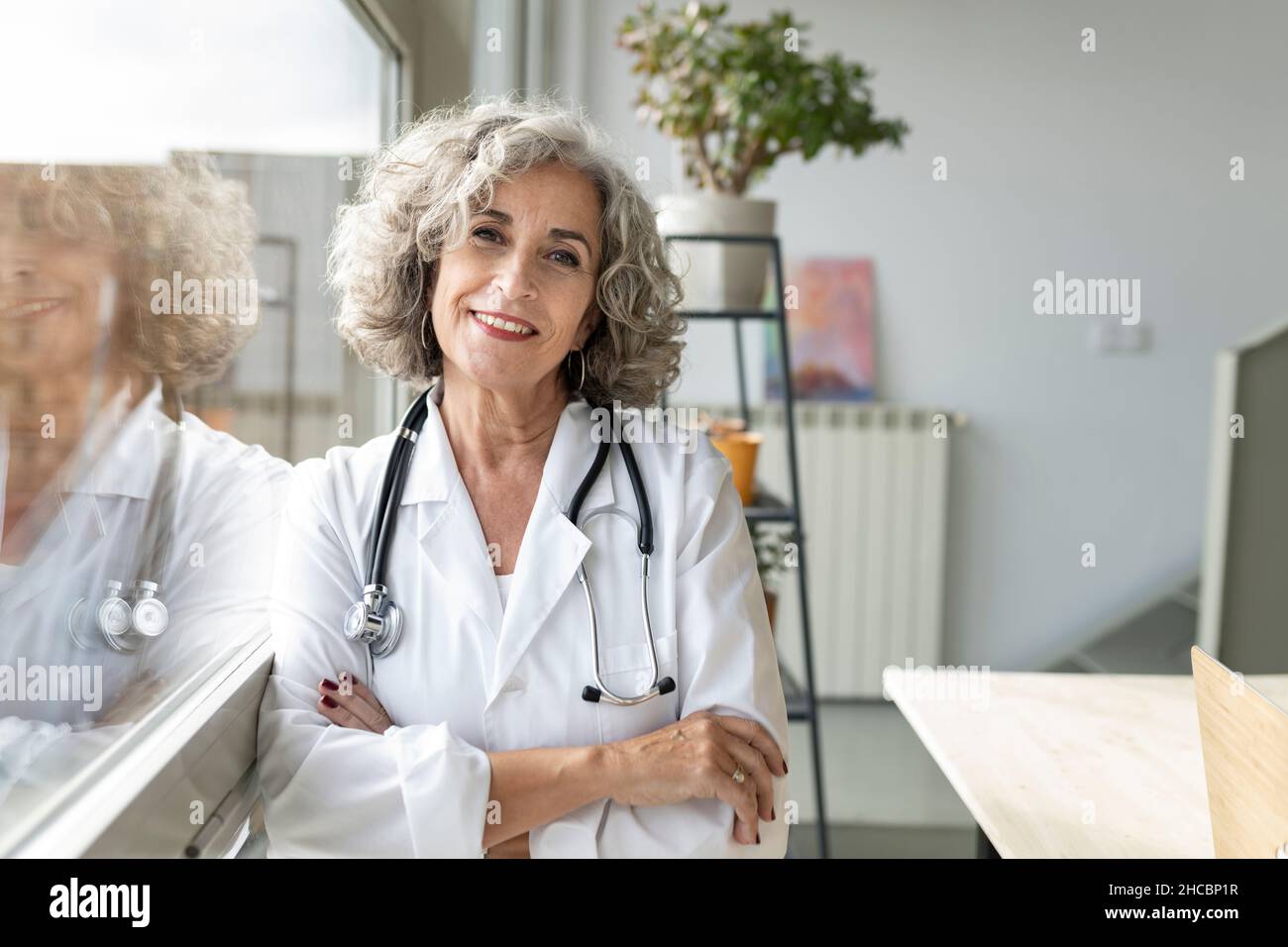 Medico esperto attento che guarda fuori attraverso la finestra a casa Foto Stock