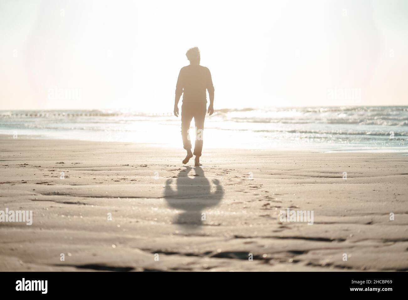 Uomo che cammina verso il mare in spiaggia Foto Stock