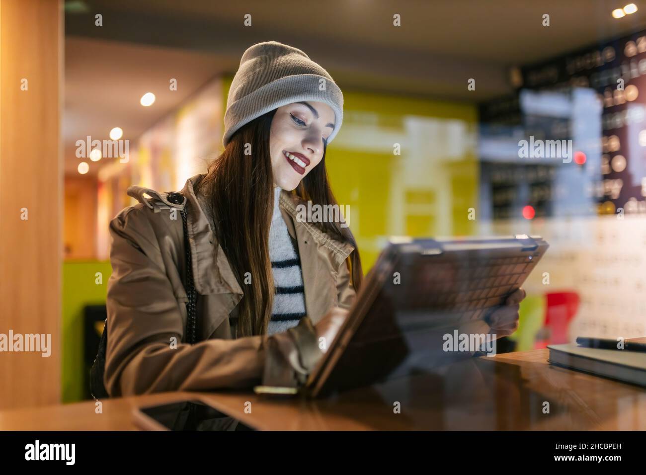 Donna che utilizza un computer portatile con schermo a sfioramento al bar visto attraverso il vetro Foto Stock