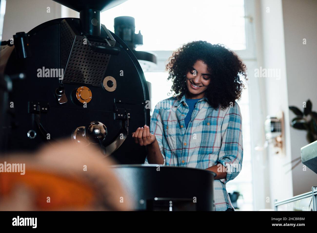 Sorridente proprietario tostare i chicchi di caffè in macchina al momento della tostatura Foto Stock