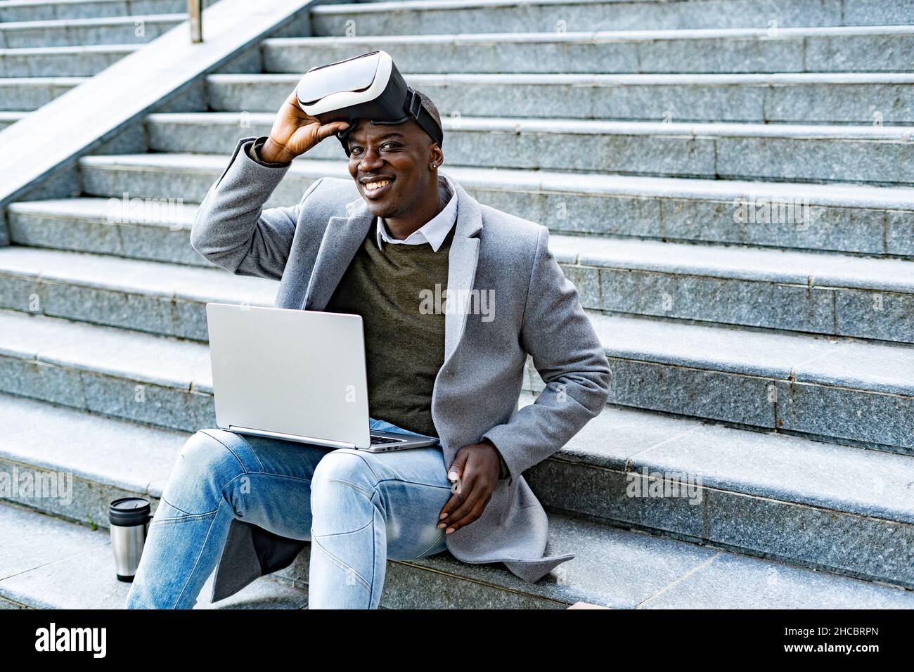 Uomo che lavora con un computer portatile seduto sui gradini Foto Stock