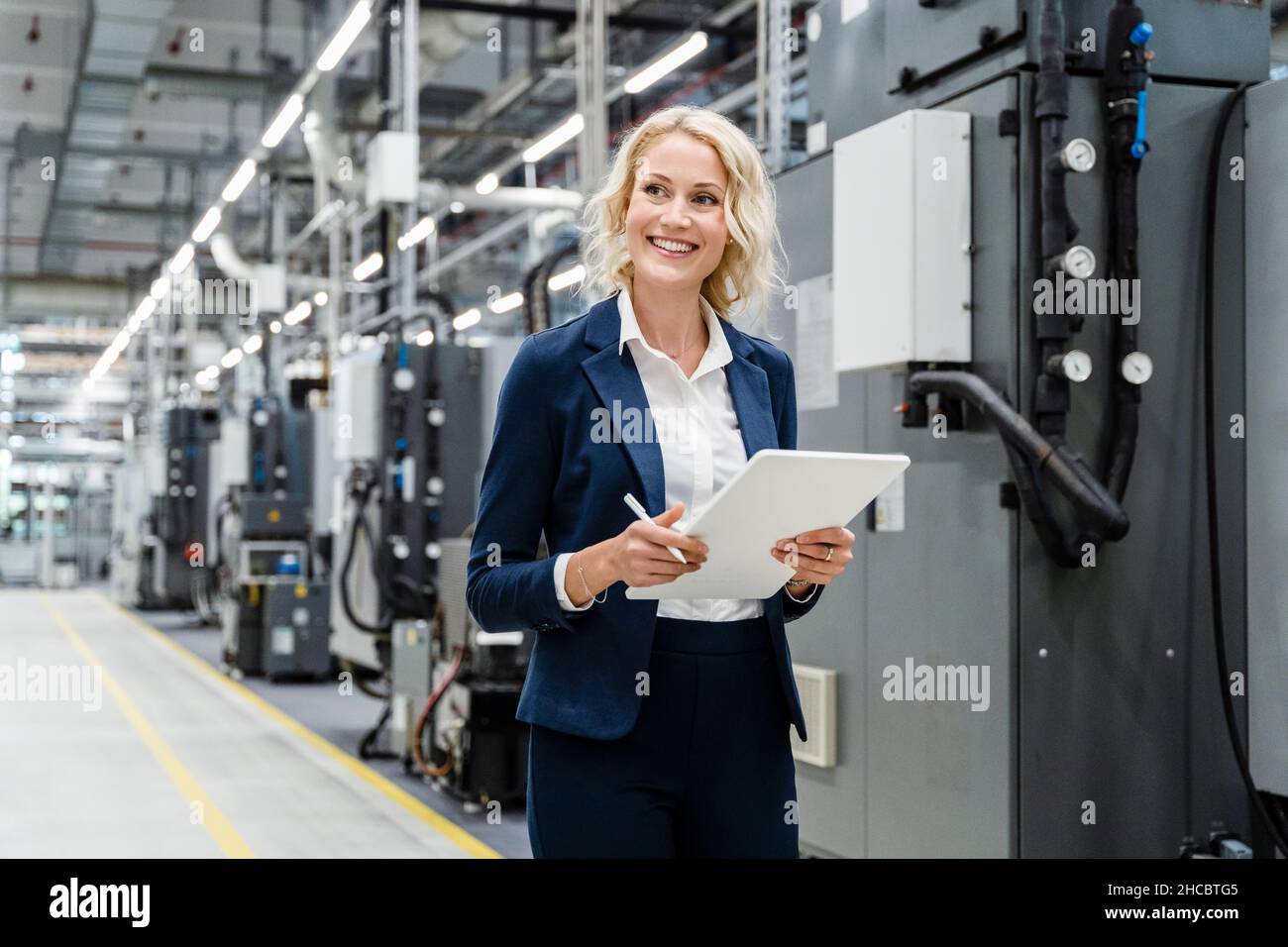 Donna d'affari sorridente con tablet PC presso apparecchiature industriali Foto Stock