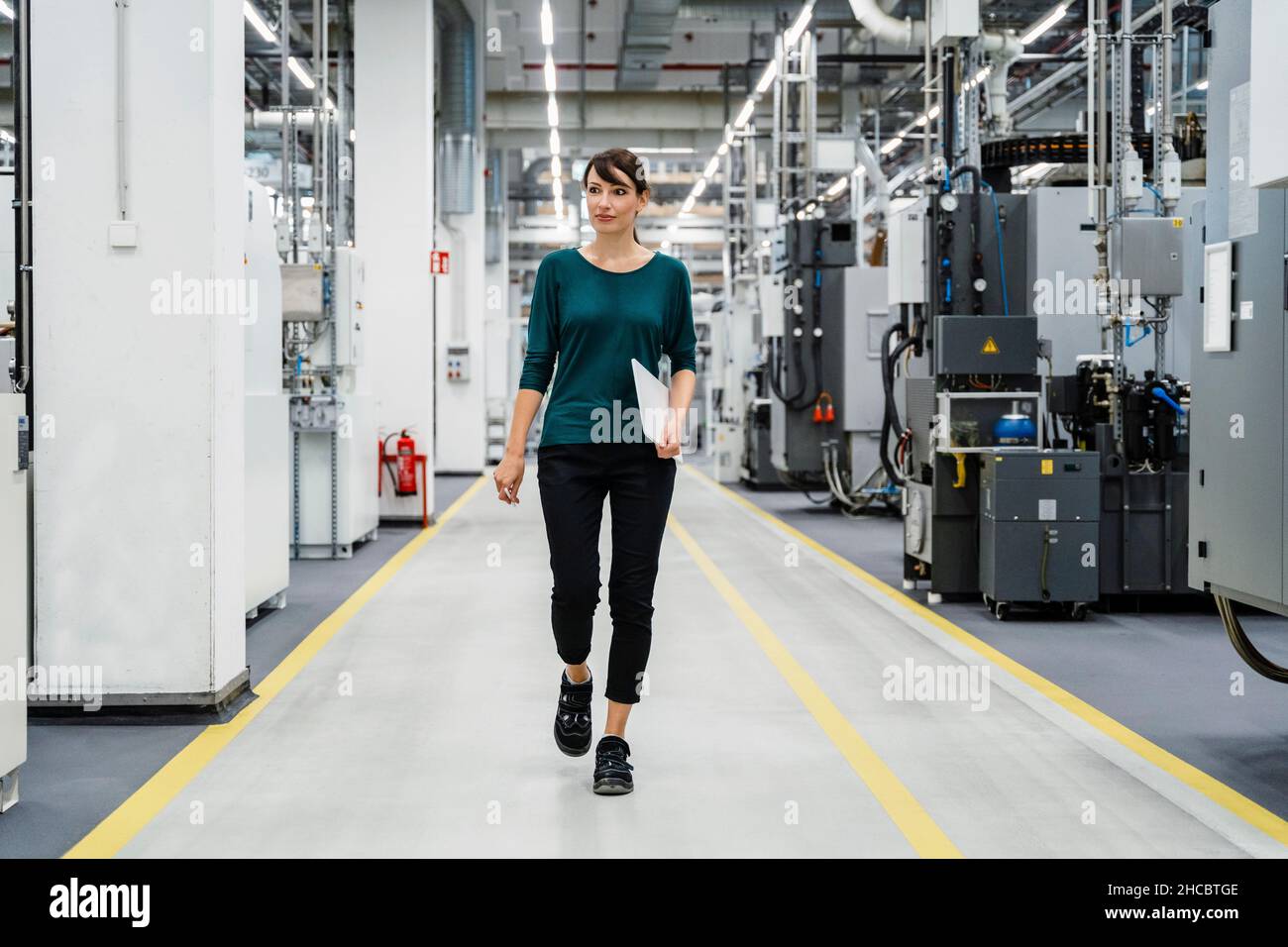 Donna d'affari con tablet PC che cammina tra le apparecchiature industriali Foto Stock
