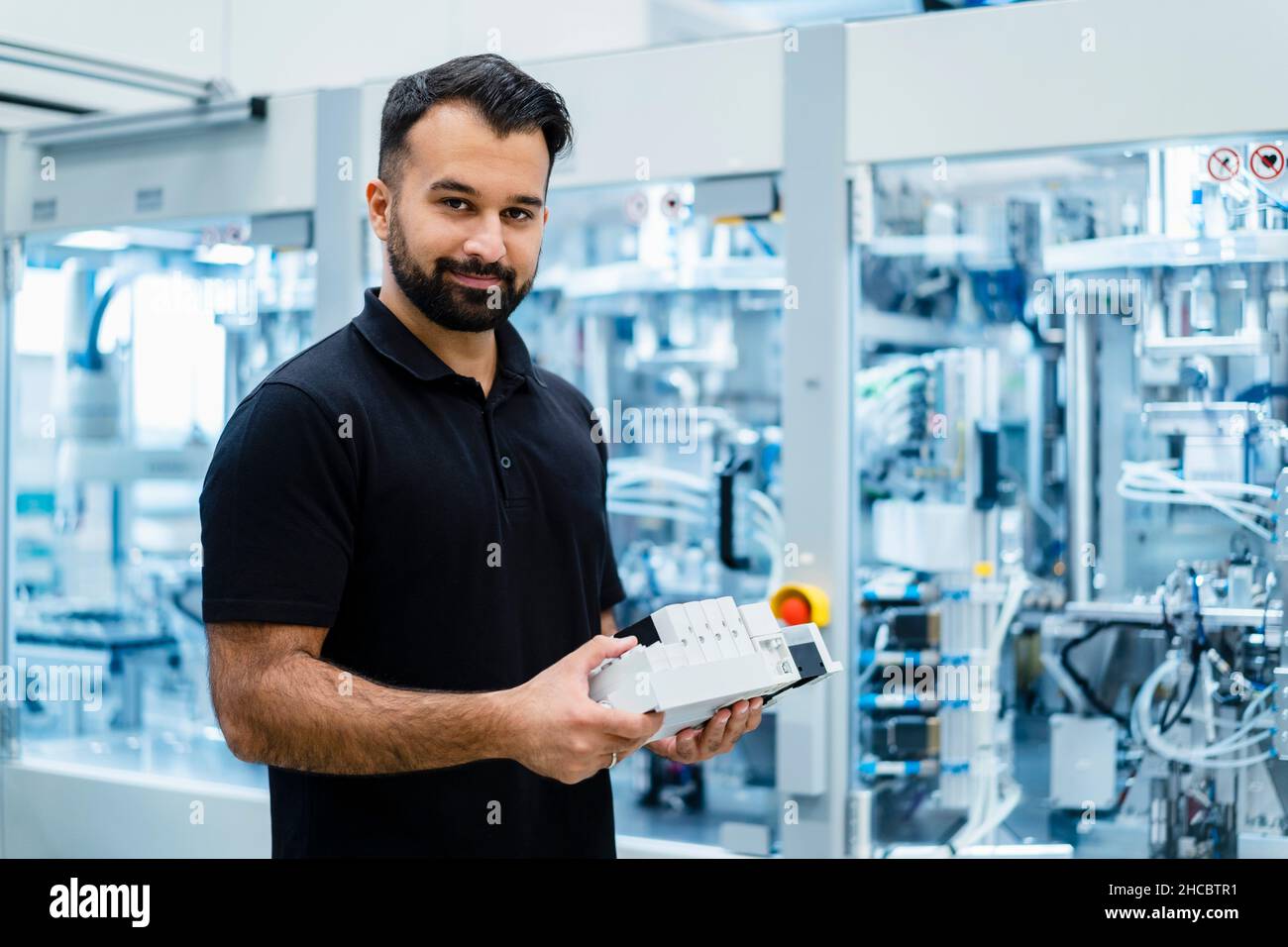 Ingegnere sorridente che tiene le apparecchiature elettriche all'industria Foto Stock