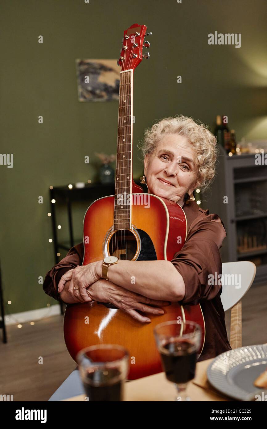 Bella donna caucasica seduta al tavolo da pranzo con chitarra acustica e guardare la macchina fotografica Foto Stock