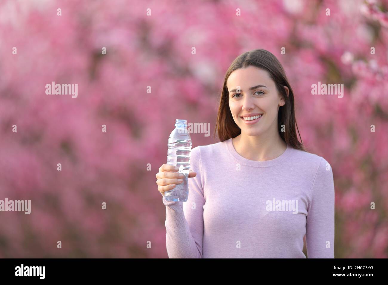 Donna felice che tiene la bottiglia d'acqua in un campo guardando la macchina fotografica Foto Stock