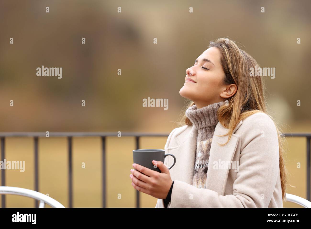 Donna felice che tiene la tazza di caffè e respirare aria fresca in inverno in una terrazza Foto Stock