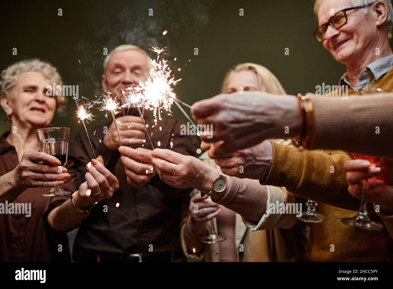 Tre donne anziane felici e due uomini di età in cerchio con scintille e occhiali in mano durante la celebrazione di Capodanno Foto Stock