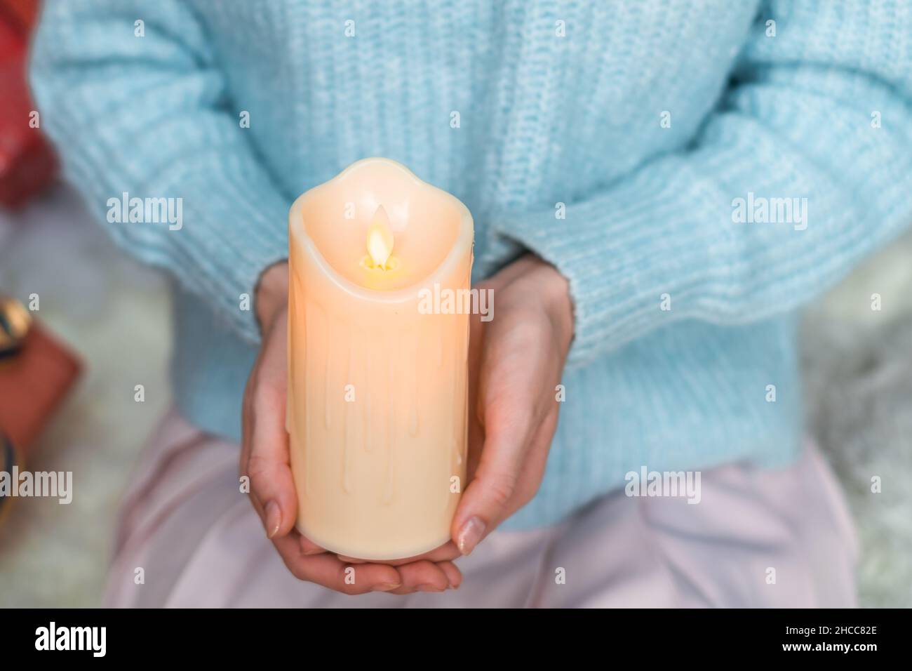 Donna in maglione azzurro tenente la candela bianca spessa della cera nelle sue mani. Vacanze di Natale. Mani femminili con candela di cera. Spazio di copia, primo piano Foto Stock