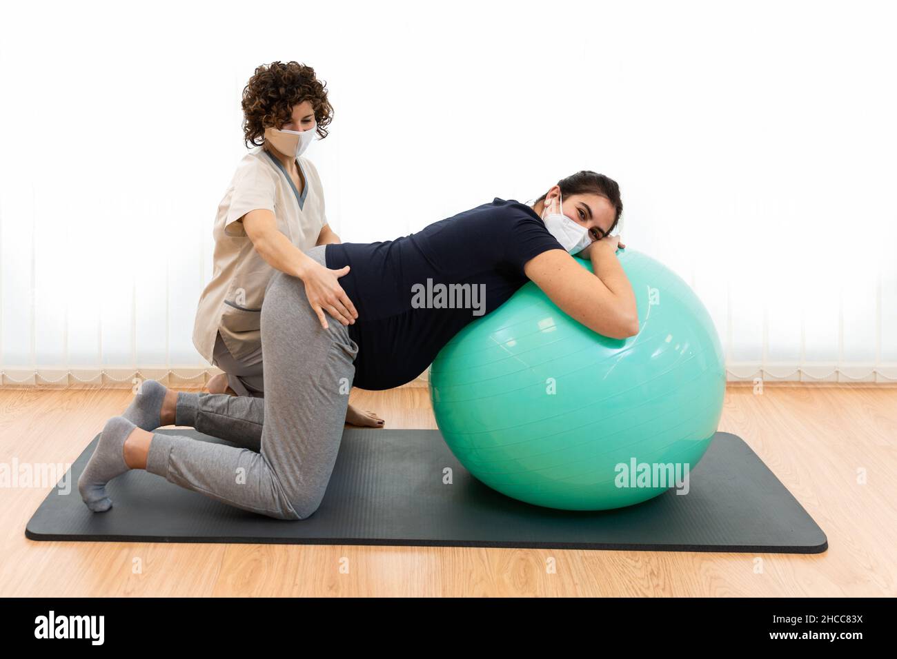 Una donna incinta che fa pilates gli esercizi con una sfera con l'aiuto del suo fisioterapista Foto Stock