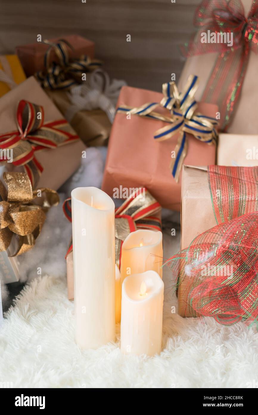 Tre spesse candele di cera bianca si erigono sul tappeto bianco accogliente vicino alle scatole regalo di Natale. Nuovo anno presenta, in carta avvolta con archi. Foto Stock