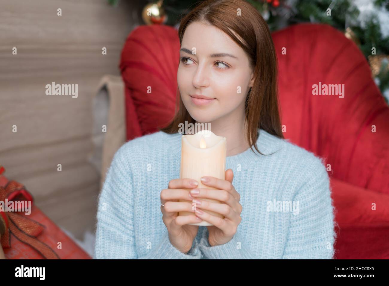 Ritratto di Capodanno della bella giovane donna caucasica in maglione azzurro con candela nelle mani. Vacanze di Natale. Foto di alta qualità Foto Stock