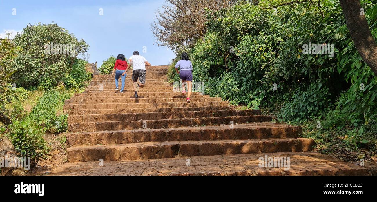 Persone che corrono sulle scale fatte con pietre di terra rosse a Elphinstone Point, Mahabaleshwar. Si stanno divertendo con il verde intorno e il cielo blu a t Foto Stock