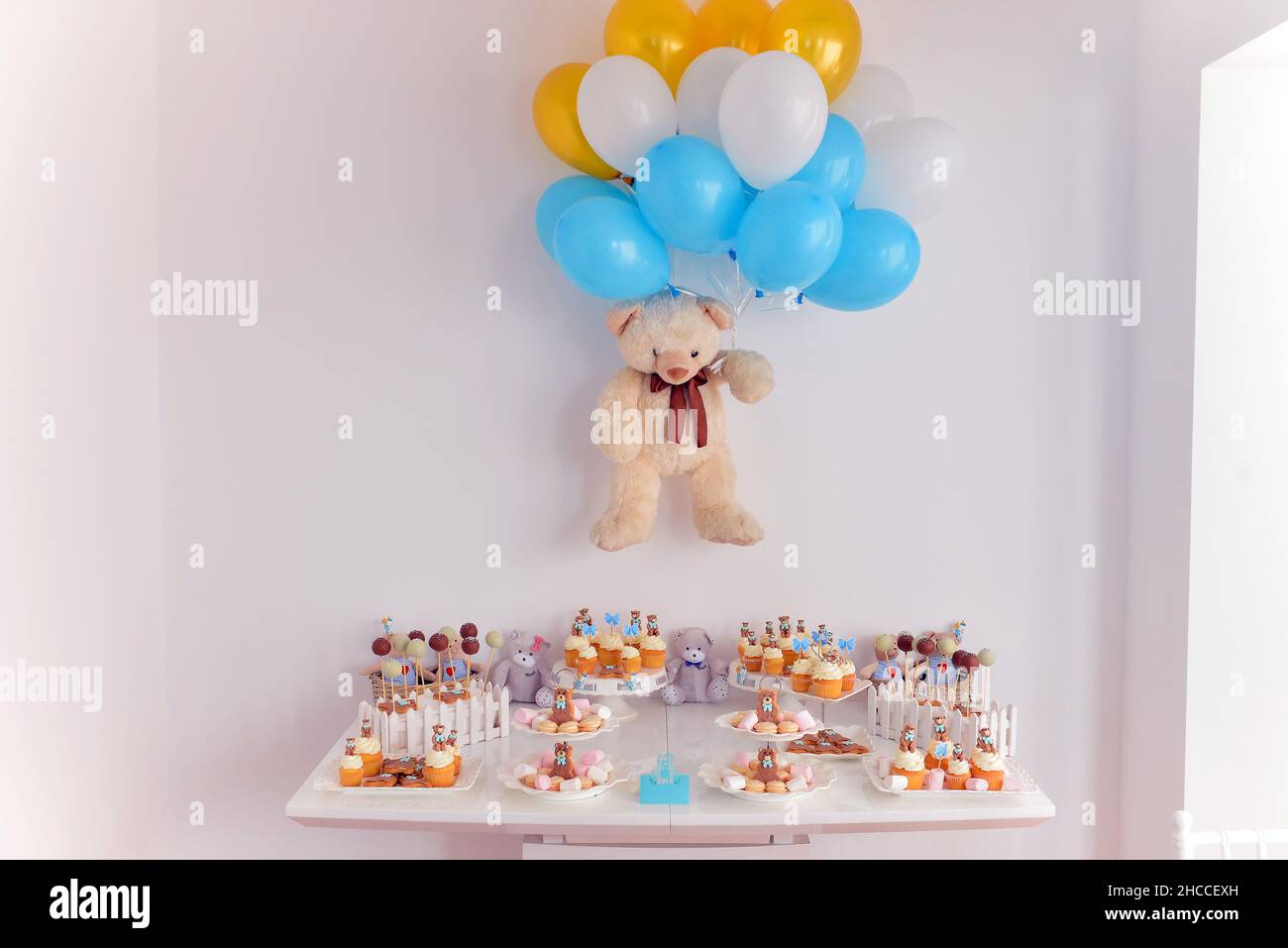 Tavolo per banchetti di cupcake splendidamente decorate con un orsacchiotto sul muro che tiene palloncini Foto Stock