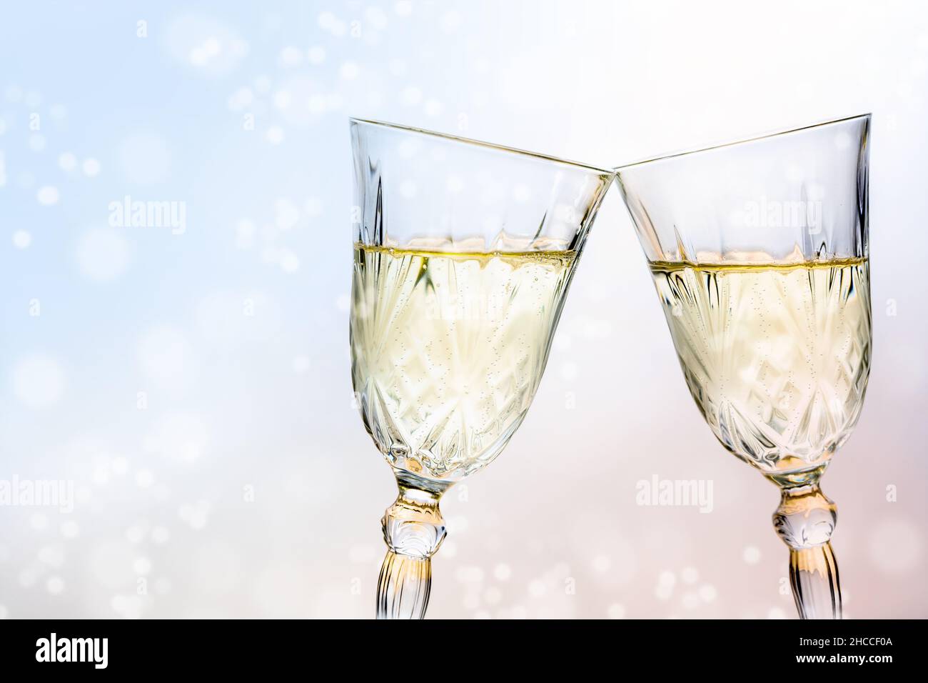 Due bicchieri di cristallo con brindisi con champagne per una festa di nuovo anno, bolle bokeh sfocate sullo sfondo chiaro, spazio copia, fuoco selezionato, profondità stretta o Foto Stock