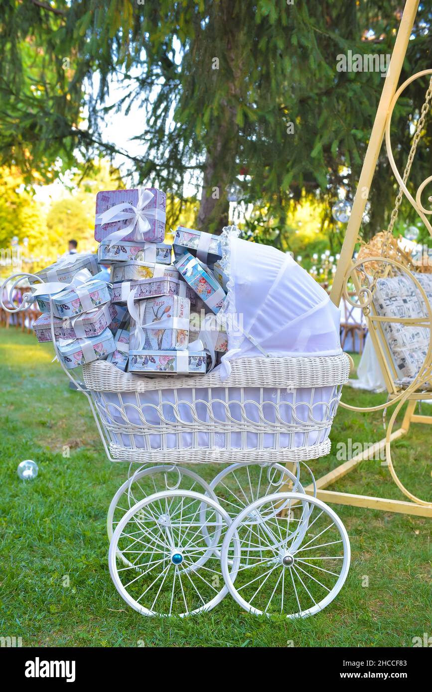 Scatto verticale di una carrozza del bambino piena di scatole del regalo in un giardino verde nell'ora d'oro Foto Stock