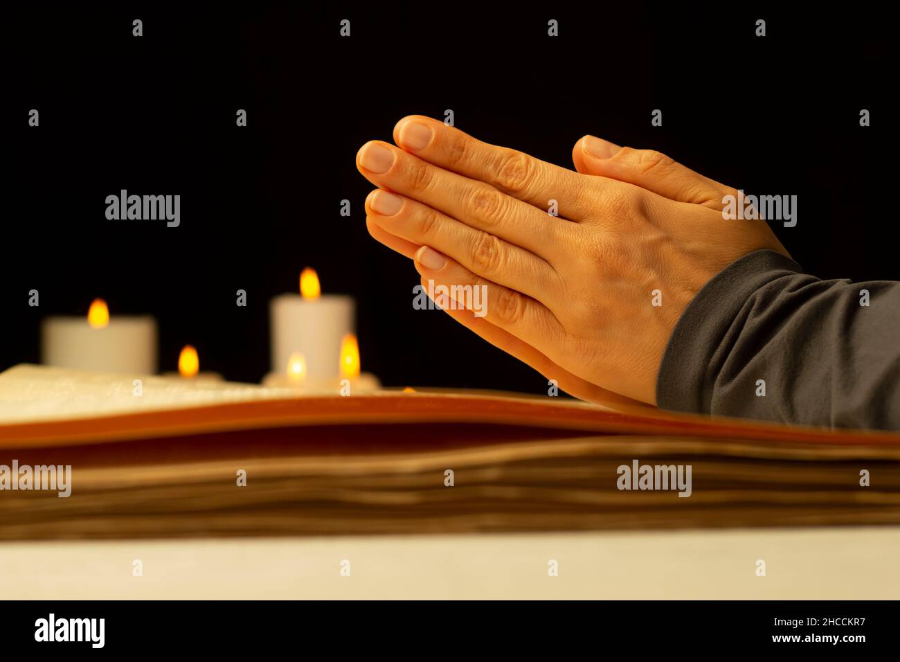 Preghiera per la benedizione. Le mani della donna sopra la bibbia sullo sfondo delle candele. Foto Stock