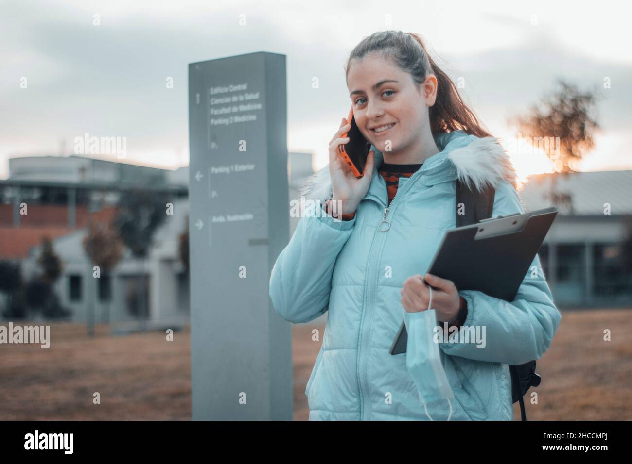 Ragazza teenage con capelli scuri che fa una telefonata al college medico con una risata felice come lei tiene le sue note e cartella Foto Stock