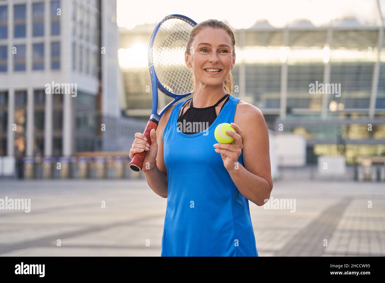 Ritratto di attraente sportivo di mezza età, professionista giocatore di tennis che tiene racket tennis e una palla pronta per giocare a tennis in città Foto Stock