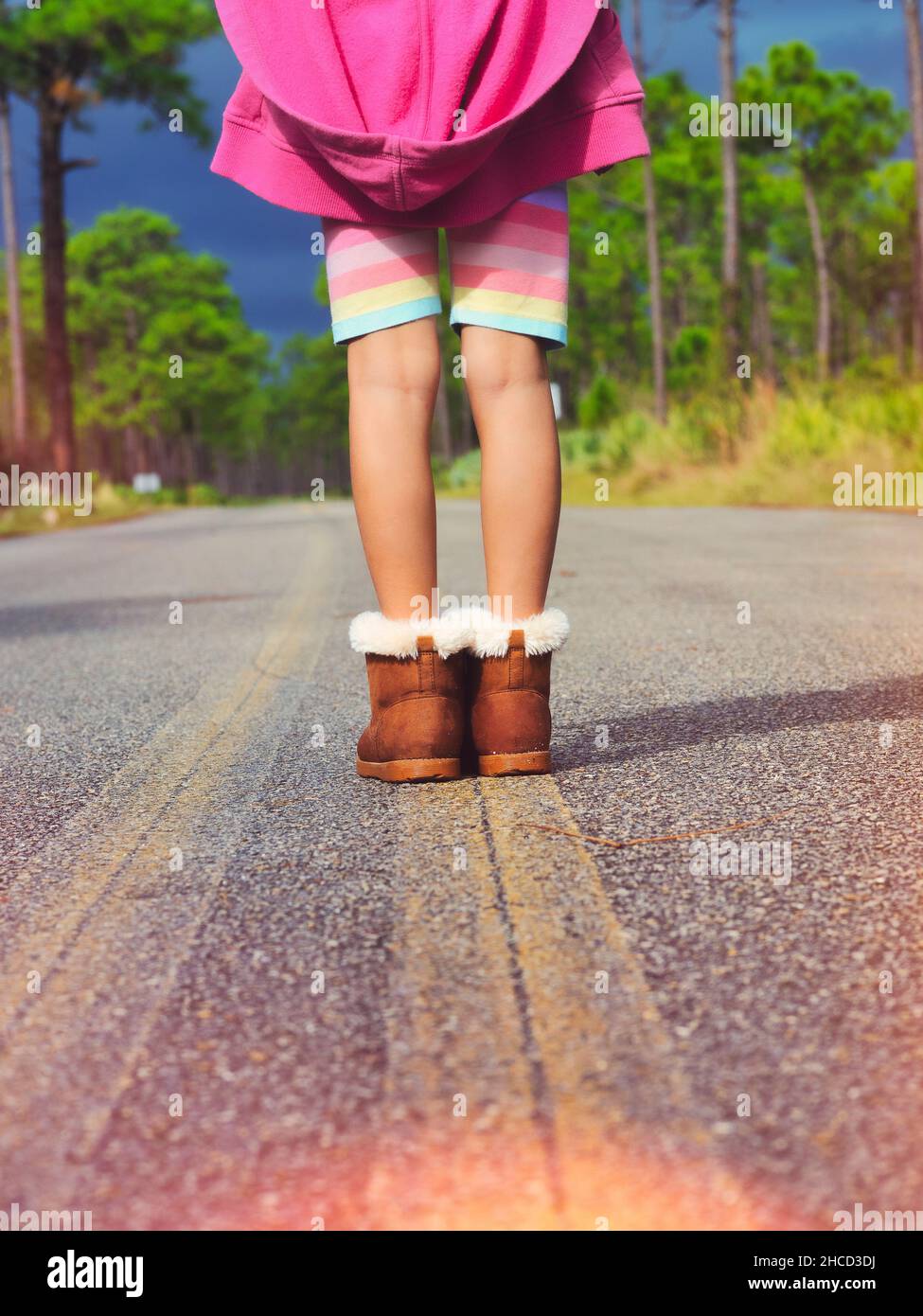 Vista posteriore verticale di un bambino in pantaloncini e stivali su una strada rurale Foto Stock