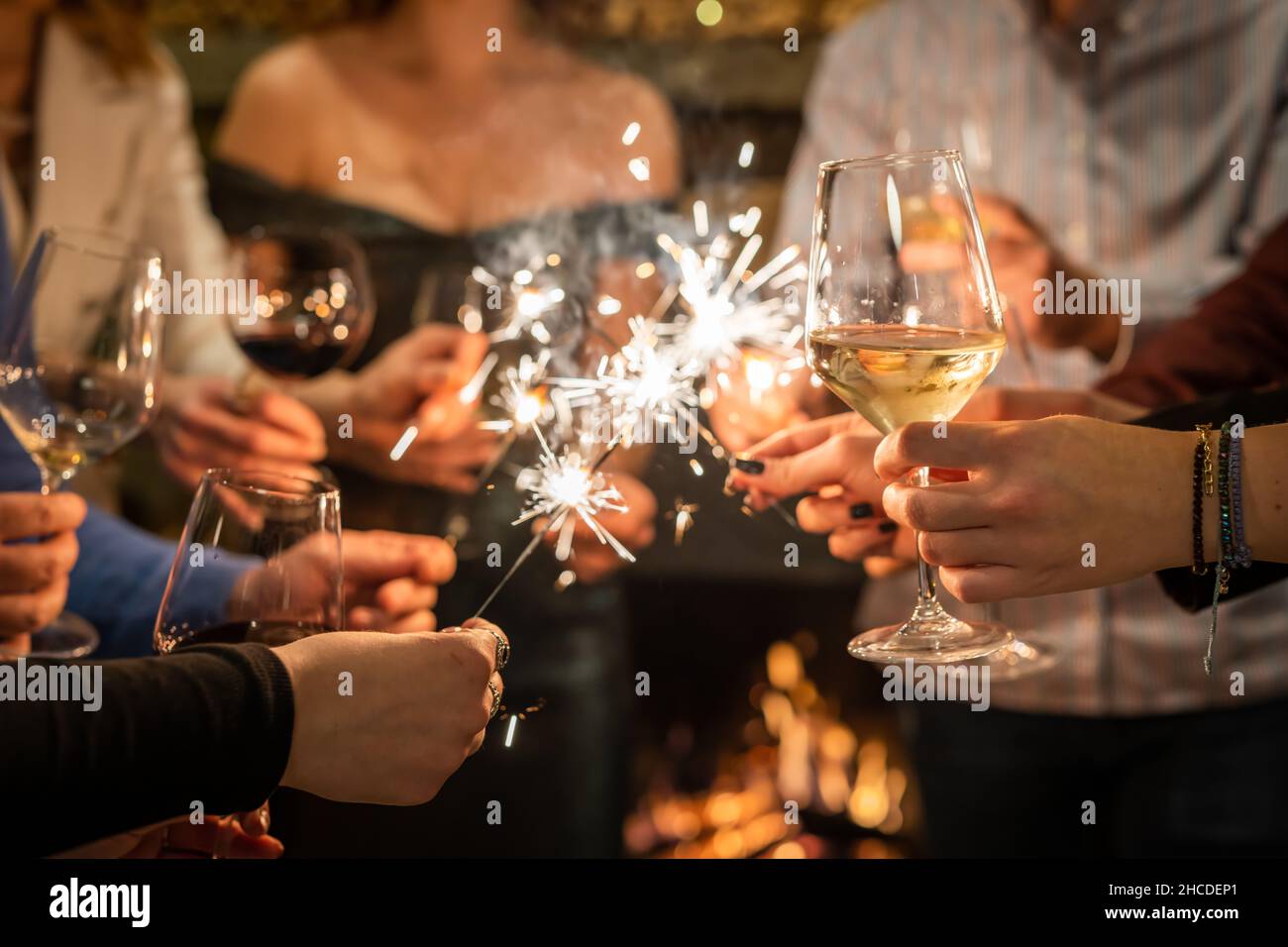 Primo piano sulle mani di un gruppo di persone che tiene bicchieri di vino e scintille durante la tostatura e la celebrazione dell'attenzione al bicchiere di vino compleanno o nuovo Foto Stock