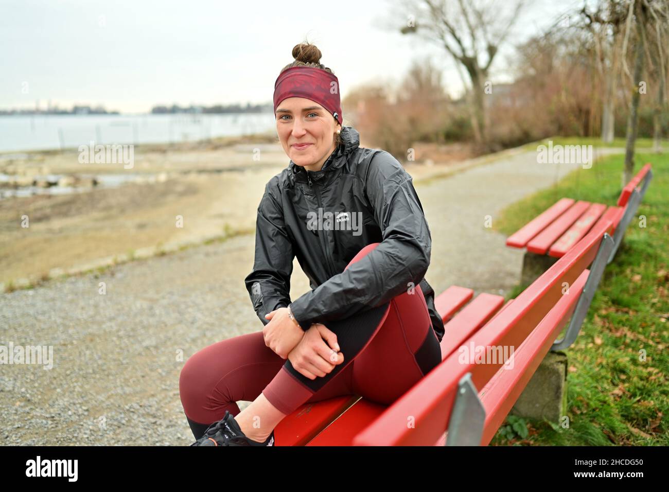 Lindau am Bodenseee, Germania. 16th Dic 2021. L'atleta Valeria Kleiner è seduto su una panchina del parco sulla riva del lago di Costanza. La città di Lindau può essere visto sullo sfondo. Kleiner ha giocato nelle selezioni DFB, ha vinto i titoli, ha giocato nella Bundesliga di calcio femminile. Le lesioni hanno causato un cambiamento. Ora compete come triathlete professionale. (To 'Triathlon dopo il calcio: Fascino e difficoltà di una carriera professionale 2nd') Credit: Felix Kästle/dpa/Alamy Live News Foto Stock