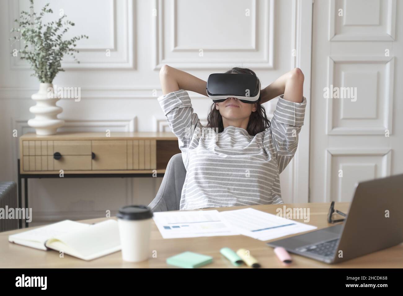 Giovane donna felice in ufficio in occhiali per realtà virtuale sul posto di lavoro, rilassarsi nel casco VR sul posto di lavoro Foto Stock