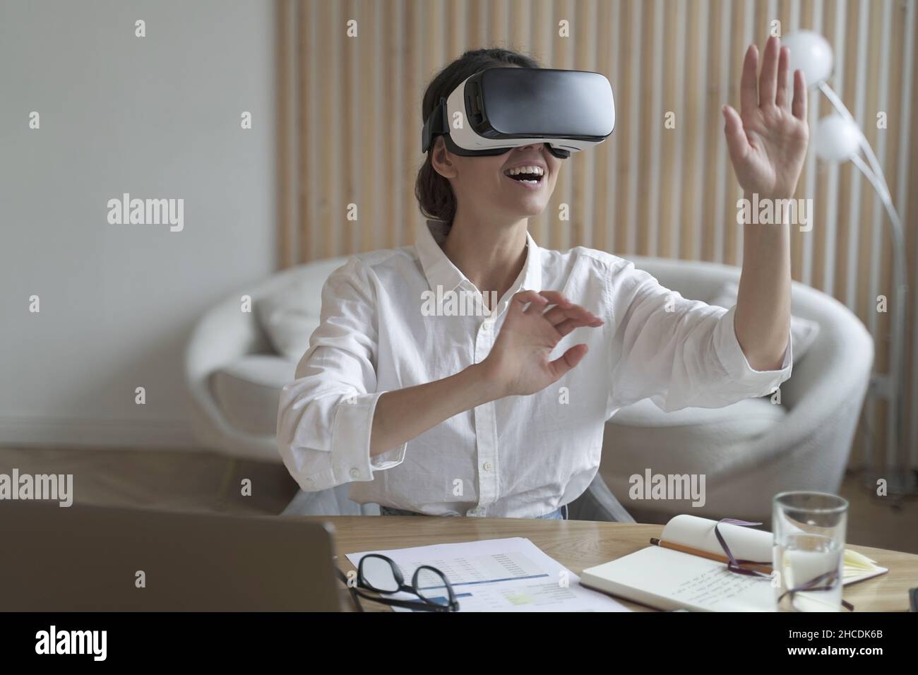 Una donna felice che lavora in ufficio e indossa occhiali di protezione per la realtà virtuale che interagiscono con la realtà virtuale sul posto di lavoro Foto Stock