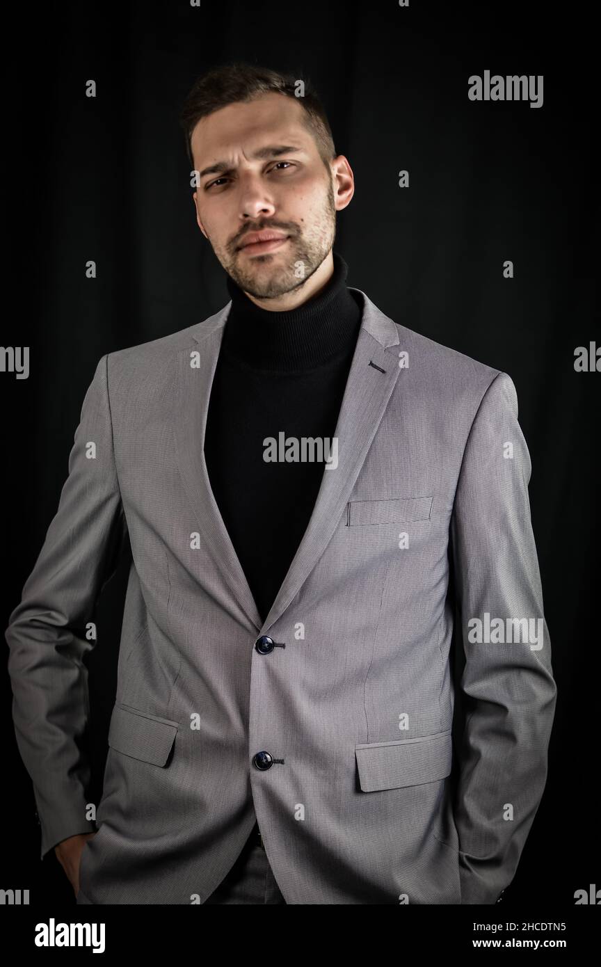 ritratto di un giovane uomo d'affari in abito grigio e dolcevita nero,  guardando serio con le mani in tasca Foto stock - Alamy