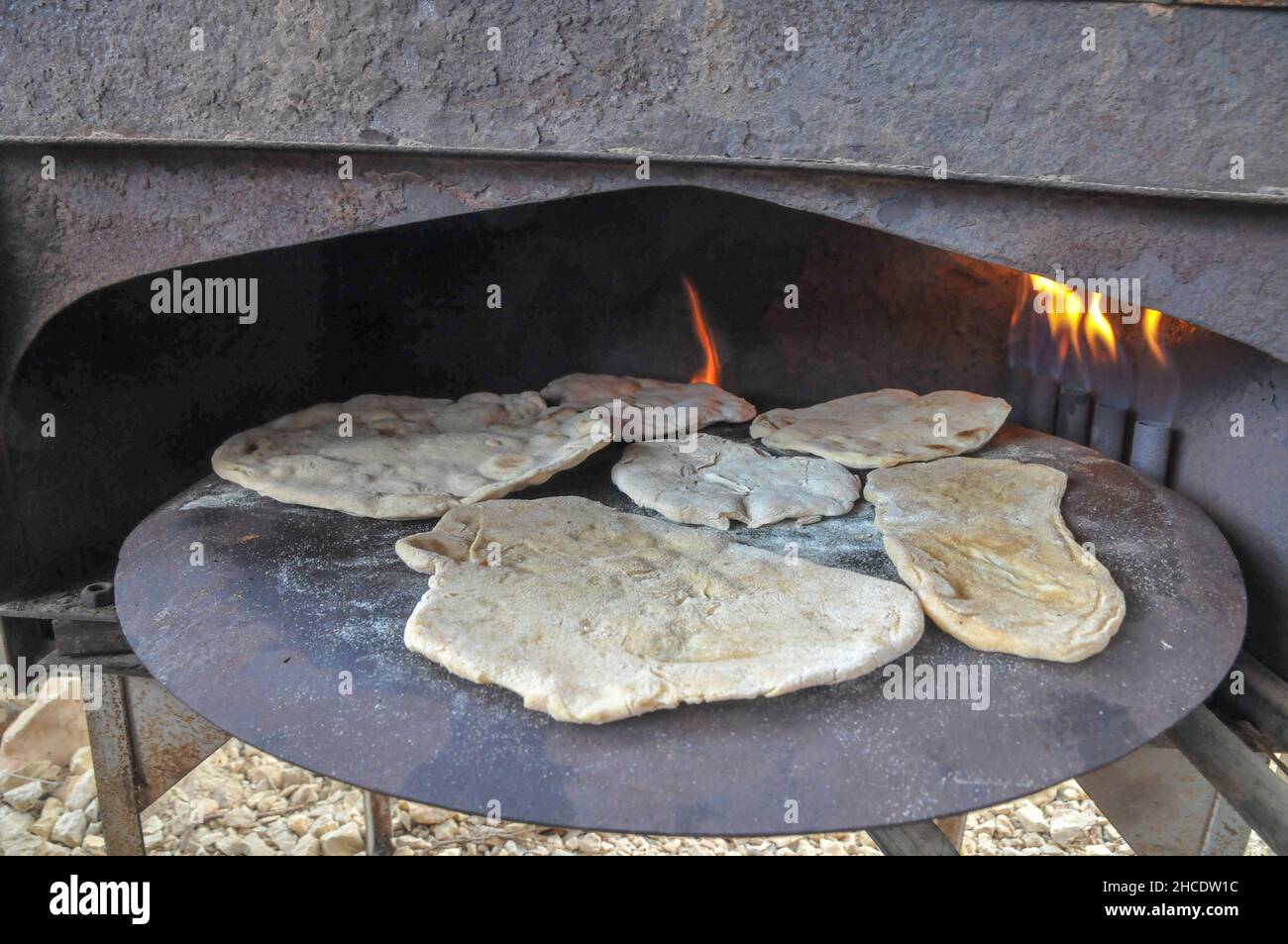 Cucina Outdoor preparare un piatto Pane Pita su un Saj - un ferro a forma di cupola pan che viene utilizzato per cuocere il pane pita. Esso è posizionato sopra una fonte di h Foto Stock