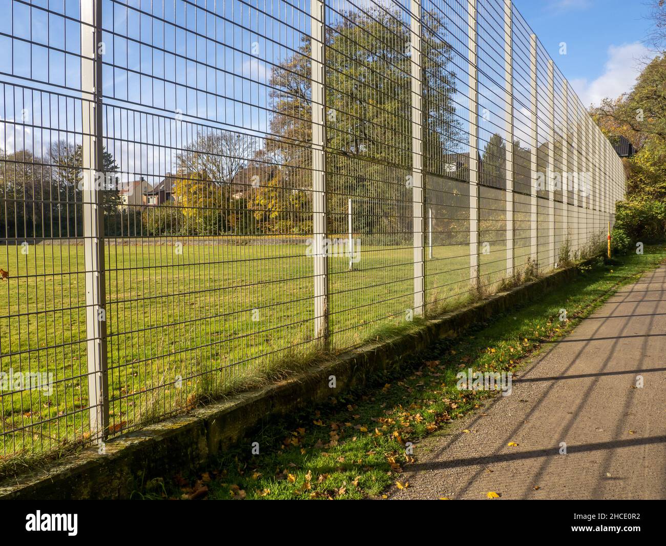 Strada vuota vicino ad un territorio verde recintato con alberi sotto un cielo blu nuvoloso in una giornata di sole Foto Stock