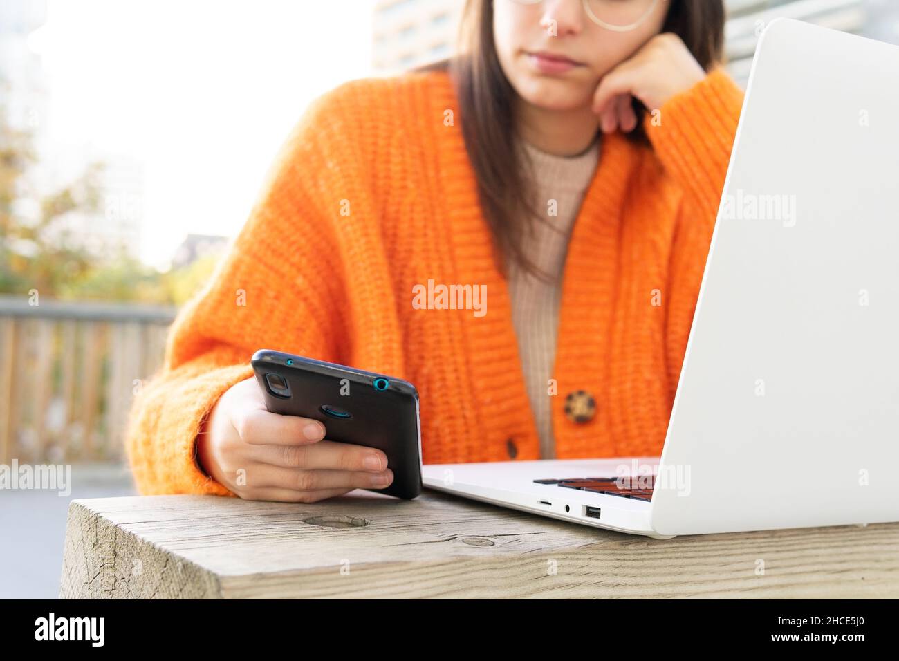 Taglia le donne freelance leggendo i messaggi sul telefono cellulare mentre lavora con il laptop in remoto nel parco Foto Stock