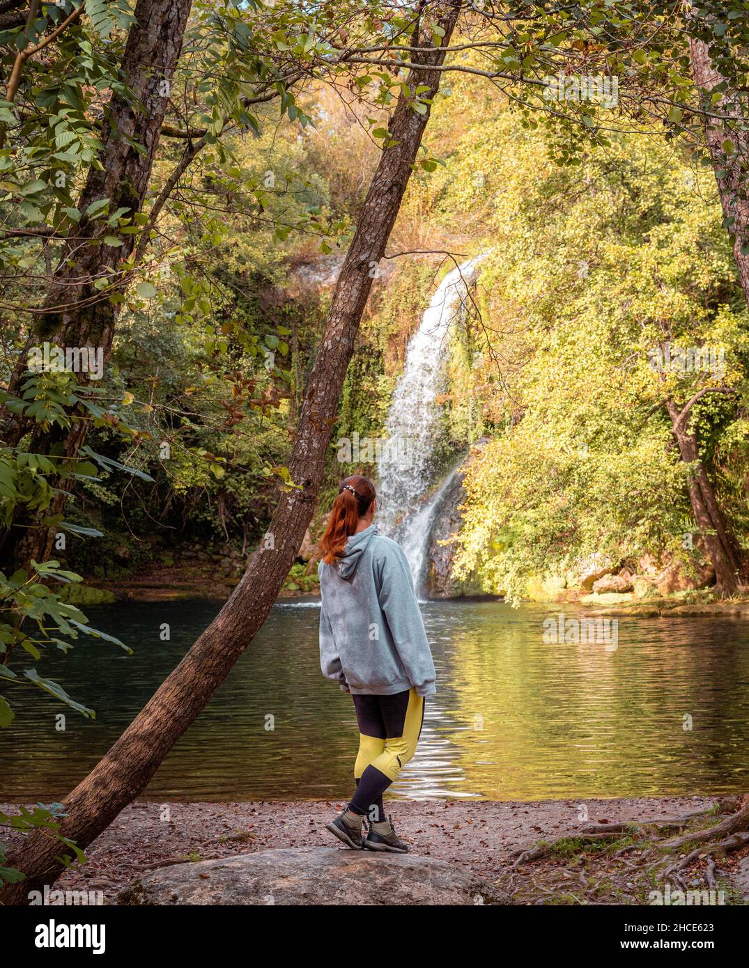 Vista posteriore dell'irriconoscibile escursionista femminile in piedi sulla riva del fiume e ammirando la cascata in Gorg de Santa Margarida Foto Stock