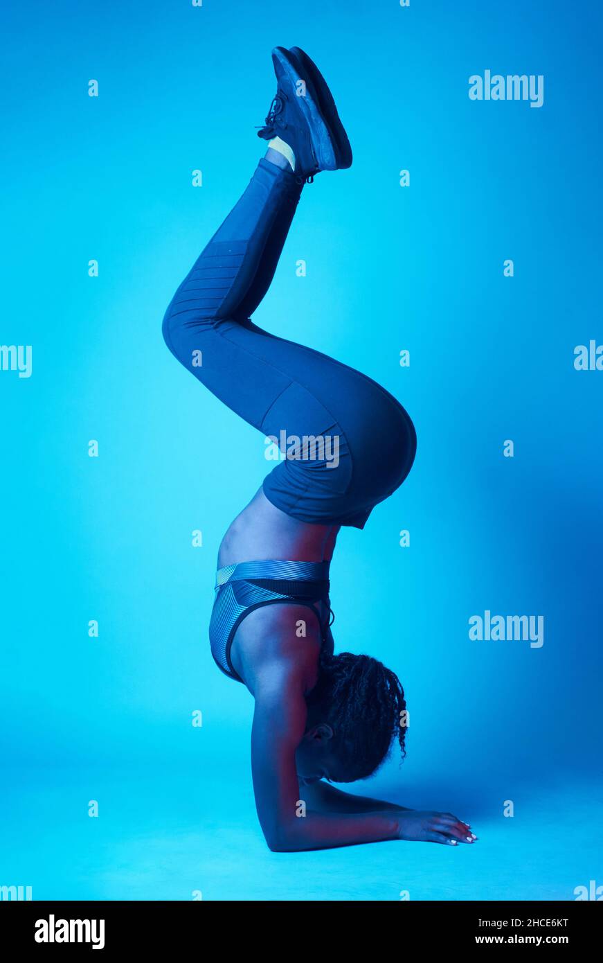 Tutta la lunghezza di sportivo etnia donna in abbigliamento sportivo facendo il cavalletto con le gambe sotto l'illuminazione blu neon in studio Foto Stock
