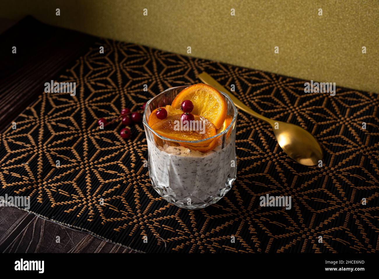 Alto angolo di calice di dessert a base di stracciatella mousse e scaglie di cioccolato sormontato da fette di arancia caramellate e frutti di bosco vicino al cucchiaio Foto Stock